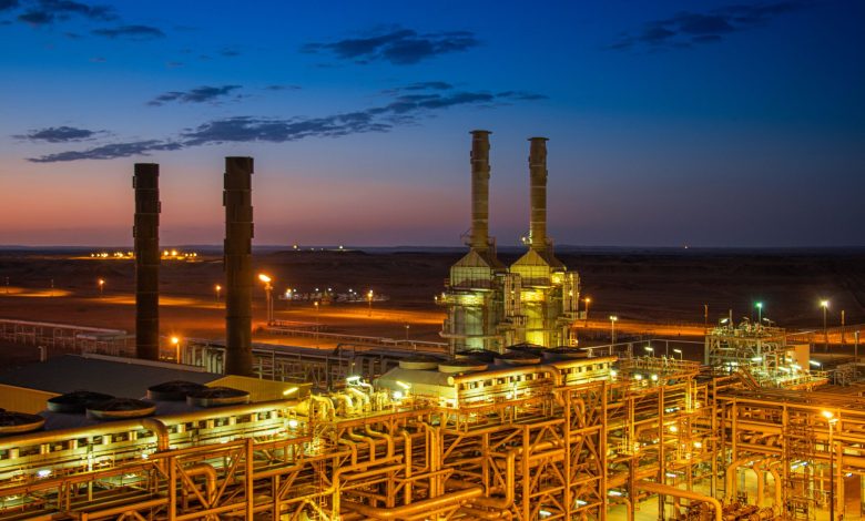 Vista aérea de uma instalação industrial iluminada ao entardecer, com edifícios e chaminés.