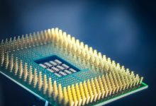 Close-up de um chip de computador com pinos dourados sobre fundo azul.