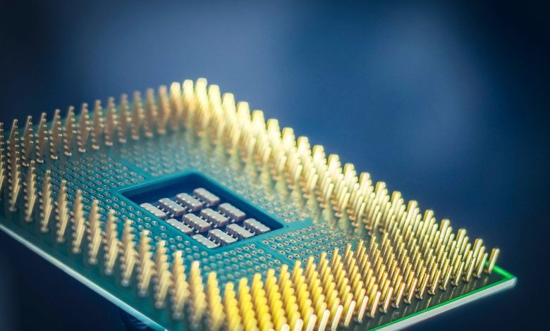 Close-up de um chip de computador com pinos dourados sobre fundo azul.