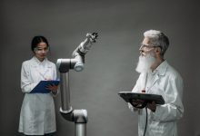 Dois pesquisadores trabalham com um braço robótico em um laboratório.
