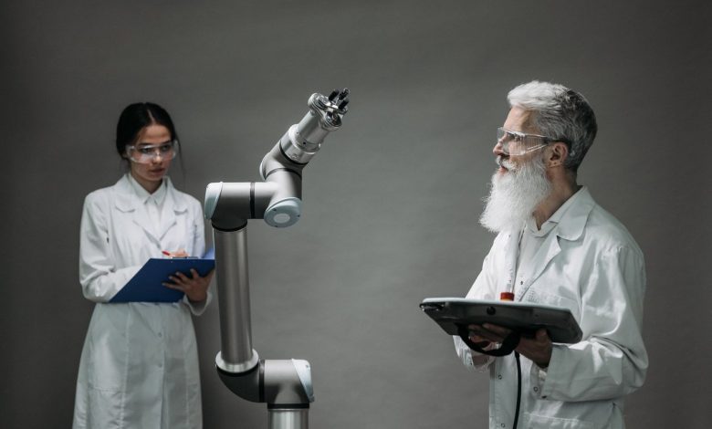 Dois pesquisadores trabalham com um braço robótico em um laboratório.