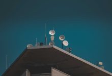 Antenas parabólicas e equipamentos de comunicação vistos de baixo contra um céu azul.