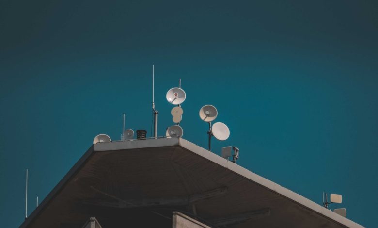 Antenas parabólicas e equipamentos de comunicação vistos de baixo contra um céu azul.