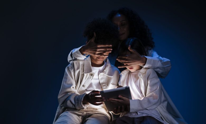 Mãe acompanha duas crianças enquanto elas usam um tablet em casa.