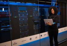 Profissional usando um laptop enquanto monitora servidores em uma moderna sala de datacenter