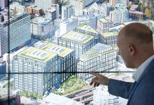 Profissional aponta para um diagrama de cidade exibido em uma tela sensível ao toque durante uma apresentação sobre planejamento urbano.
