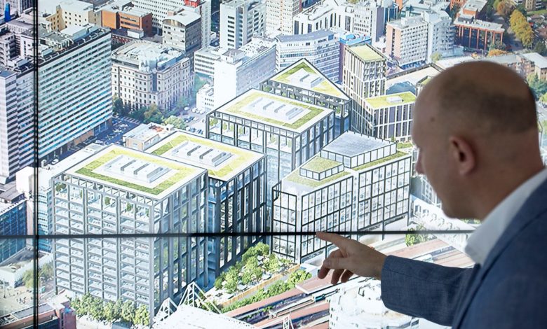 Profissional aponta para um diagrama de cidade exibido em uma tela sensível ao toque durante uma apresentação sobre planejamento urbano.