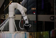 Braço robótico branco operando em uma instalação industrial moderna.