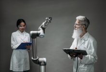 Dois pesquisadores trabalham juntos diante de um braço robótico em um laboratório de tecnologia.