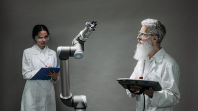 Dois pesquisadores trabalham juntos diante de um braço robótico em um laboratório de tecnologia.