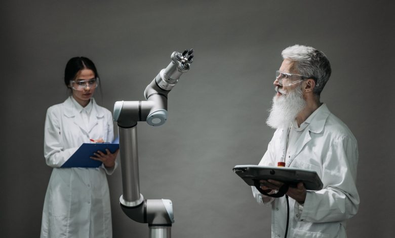 Dois pesquisadores trabalham juntos diante de um braço robótico em um laboratório de tecnologia.