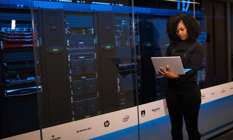 Profissional usando um laptop enquanto monitora servidores em uma moderna sala de datacenter